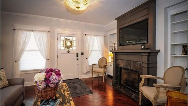 A living room with a fireplace, a sofa, a coffee table with a basket, and a television mounted on the wall. - Historic Bradshaw House (Jacksonville)