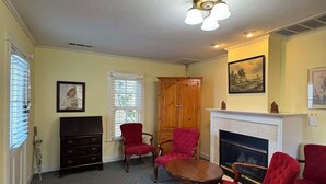 A living room with a fireplace, red chairs, a wooden cabinet, and a ceiling light fixture. - Cottage Nine in Jacksonville (Jacksonville)