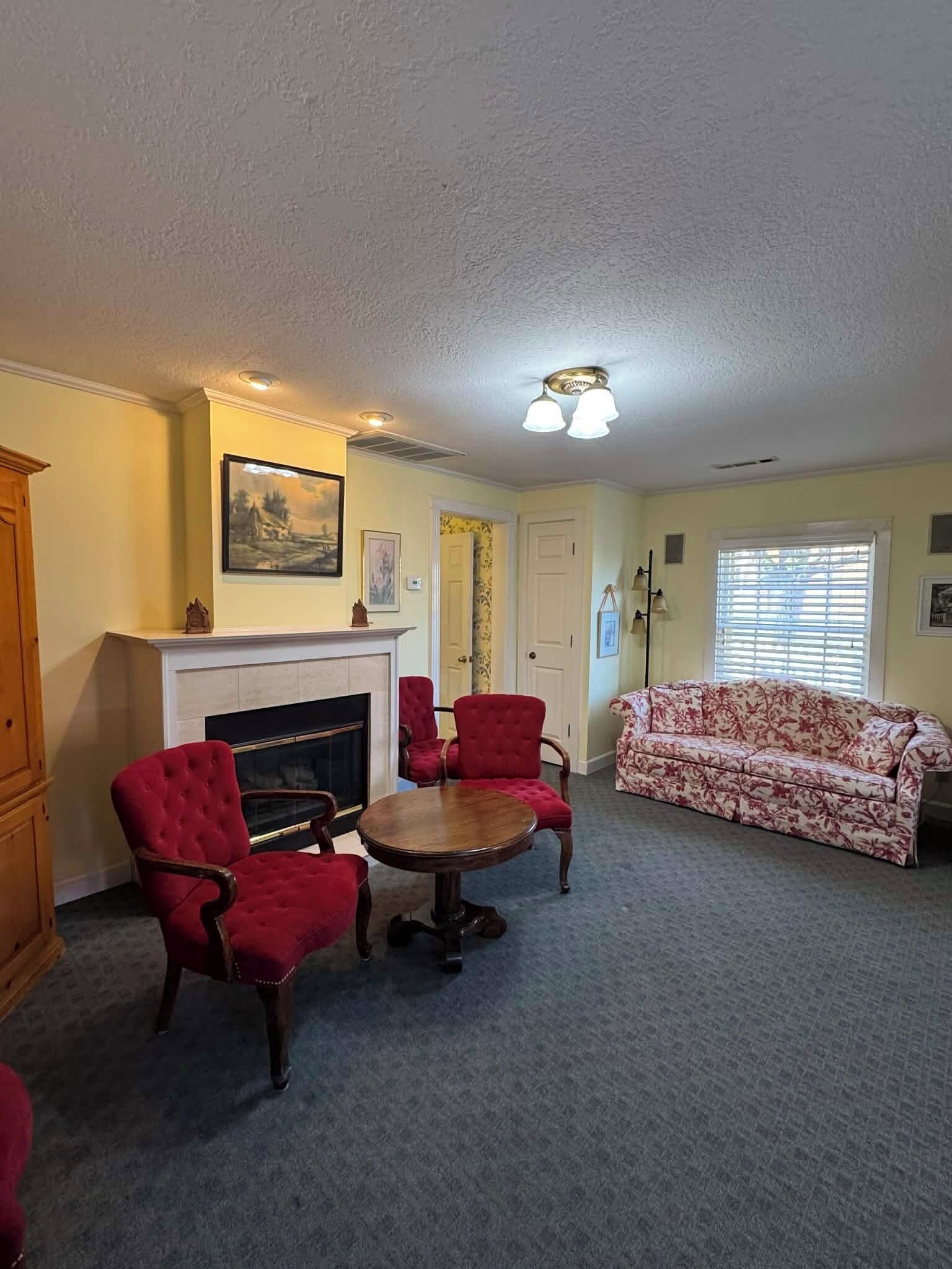 Ein Wohnzimmer mit Kamin, roten Sesseln, einem blumigen Sofa und einem runden Tisch.