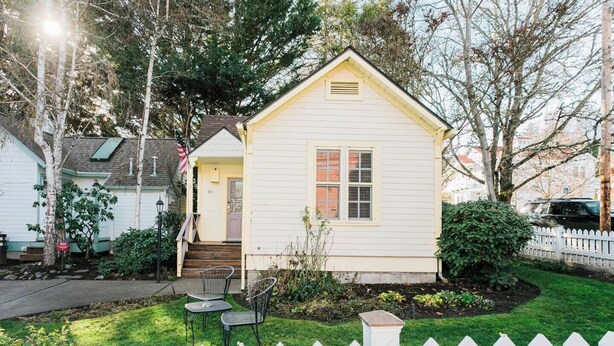 A small, single-story house with a front porch, a white picket fence, and a well-maintained lawn. - Cottage Nine in Jacksonville (Jacksonville)