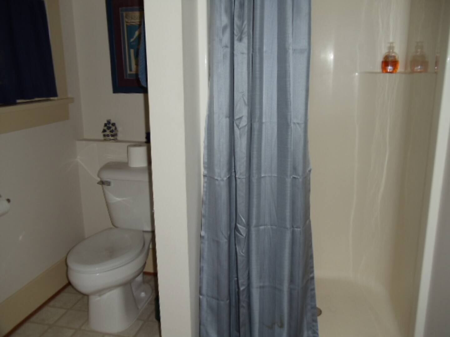 A bathroom with a toilet, a shower curtain, and a shelf with toiletries.