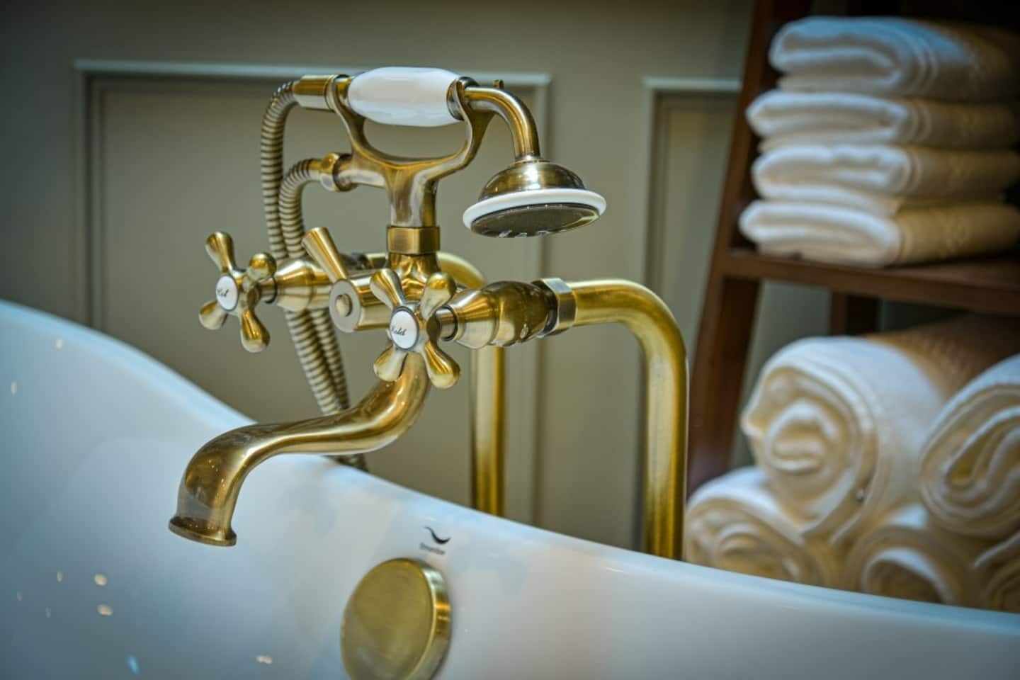 A bathtub with a brass faucet and shower head, and a towel rack in the background.