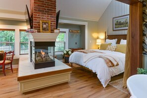 A bedroom with a fireplace, a bed with white bedding, and a view of greenery outside. - Cottage Eleven in Jacksonville (Jacksonville)