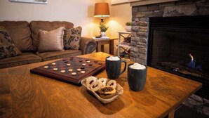 Een gezellige woonkamer met een houten salontafel, een bordspel met geruit patroon, twee mokken en een mandje koekjes.