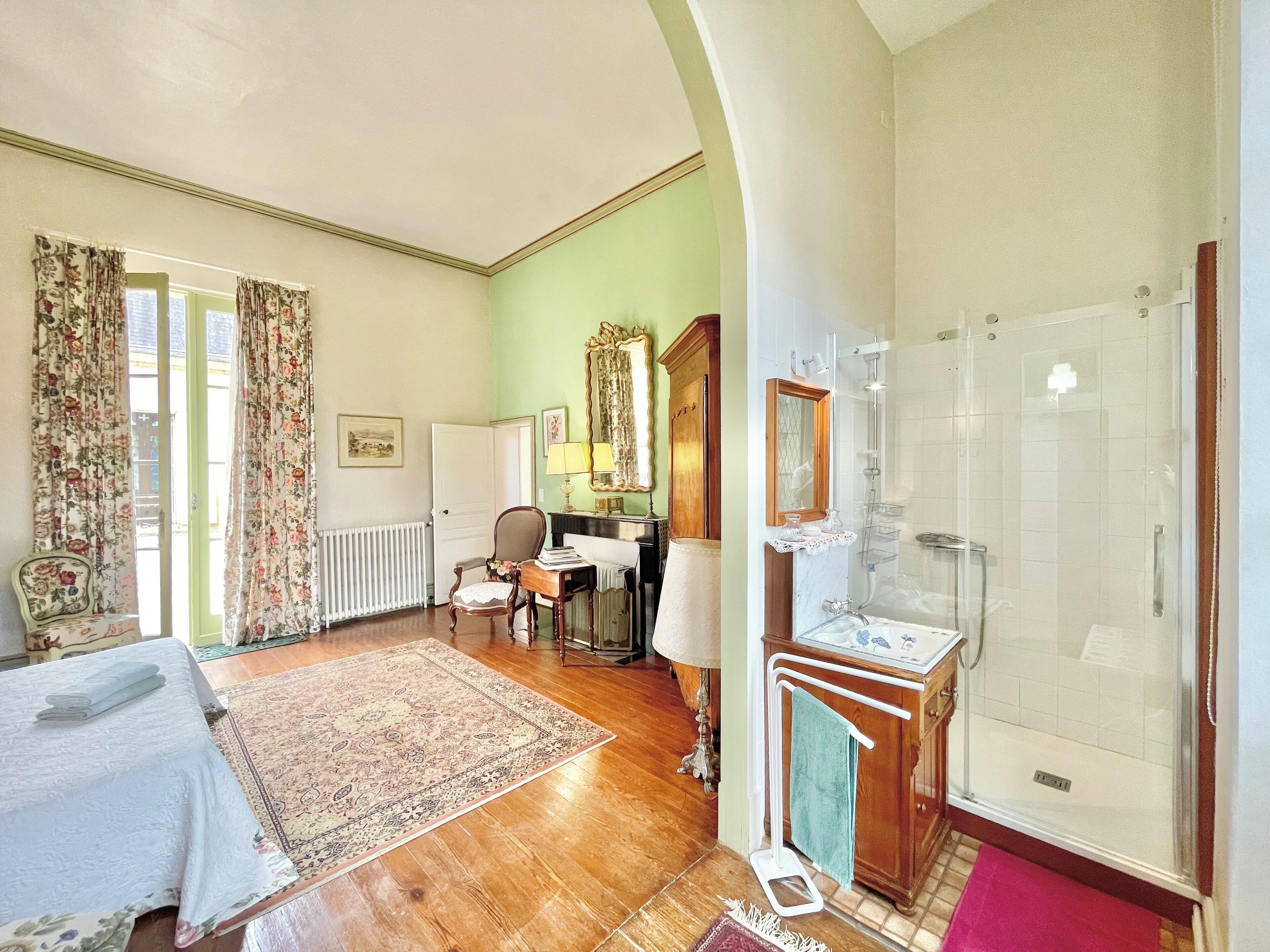 Une pièce spacieuse avec un grand lit, un coin salon comprenant une chaise et une table, une salle de bain avec douche et lavabo, et un mur végétal.