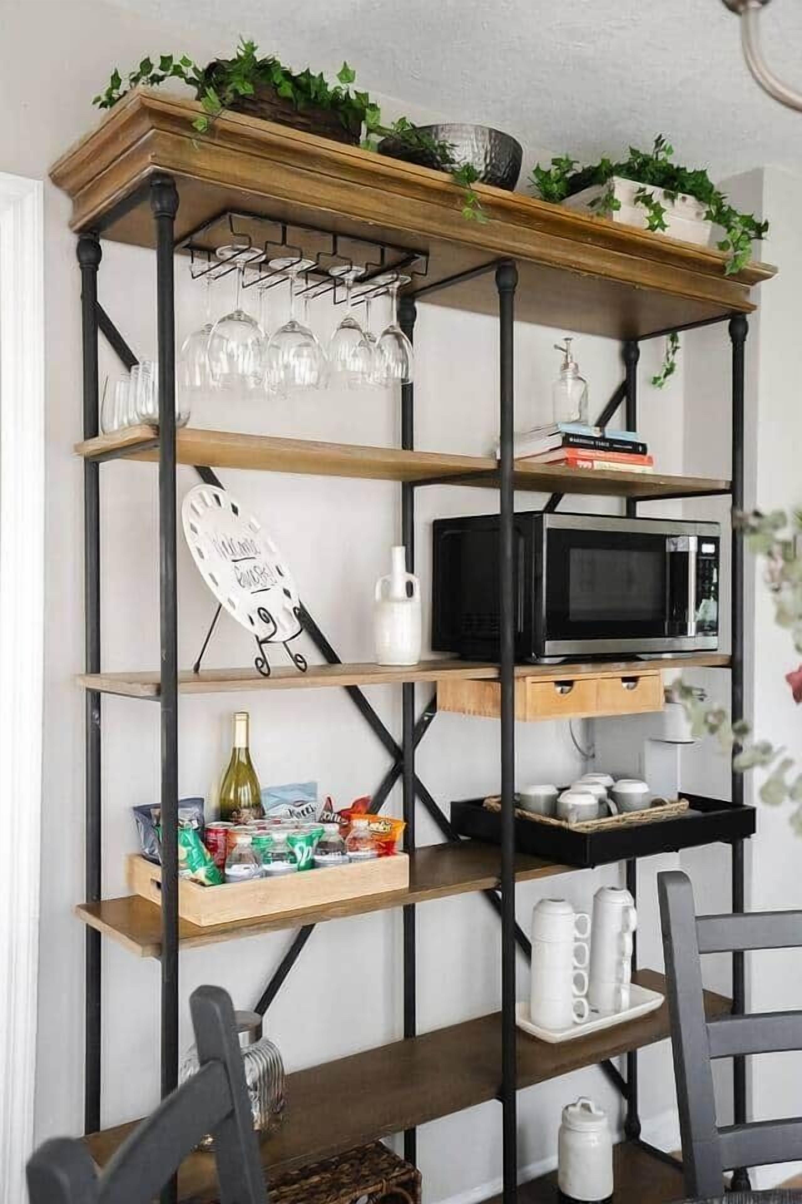 A kitchen with a wooden shelf unit holding various items, including a microwave, wine glasses, and kitchenware.
