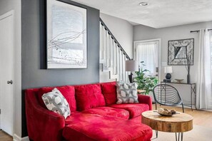 Una sala de estar con un sofá rojo, una mesa de centro redonda de madera y una escalera.