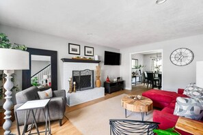 Una sala de estar moderna con chimenea, un comedor y una cocina visibles a través de un ventanal.