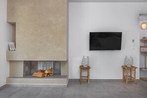 A modern living room with a fireplace, a mounted TV, and two decorative vases on wooden stools. - Villa-Pastida (Rhodes)