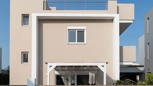 Un edifici modern amb teulada plana, un balcó i una entrada coberta amb una banca.
