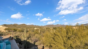 Wüstenlandschaft mit Bergen im Hintergrund, einem Poolbereich und vereinzelter Vegetation.