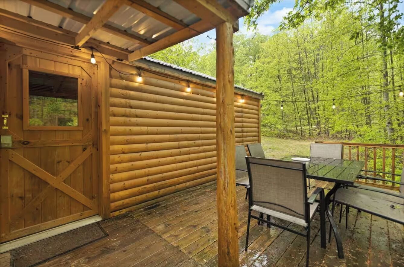 A wooden cabin with a covered porch, a dining table, and chairs.