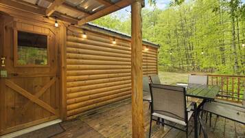 A wooden cabin with a covered porch, a dining table, and chairs.