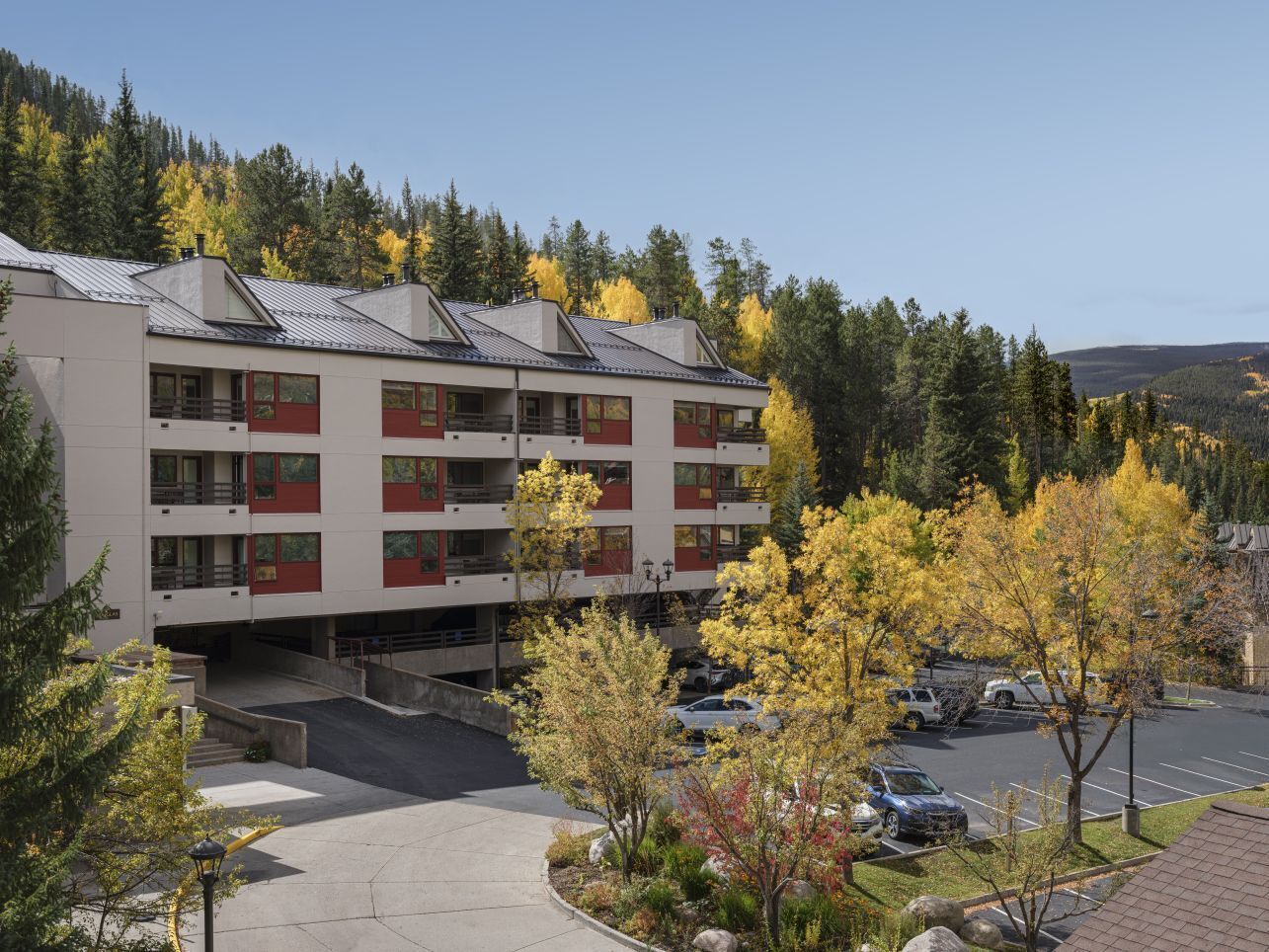 A multi-story hotel with a parking area and autumn foliage.