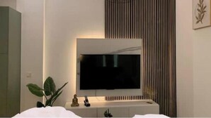Een moderne hotelkamer met een grote flatscreen televisie aan de muur, een nachtkastje met een plant en een decoratief paneel boven de televisie.