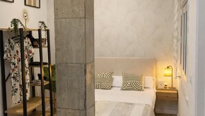 Een slaapkamer met een bed, een nachtkastje, een vloerlamp, een plafondventilator en een grote zuil.
