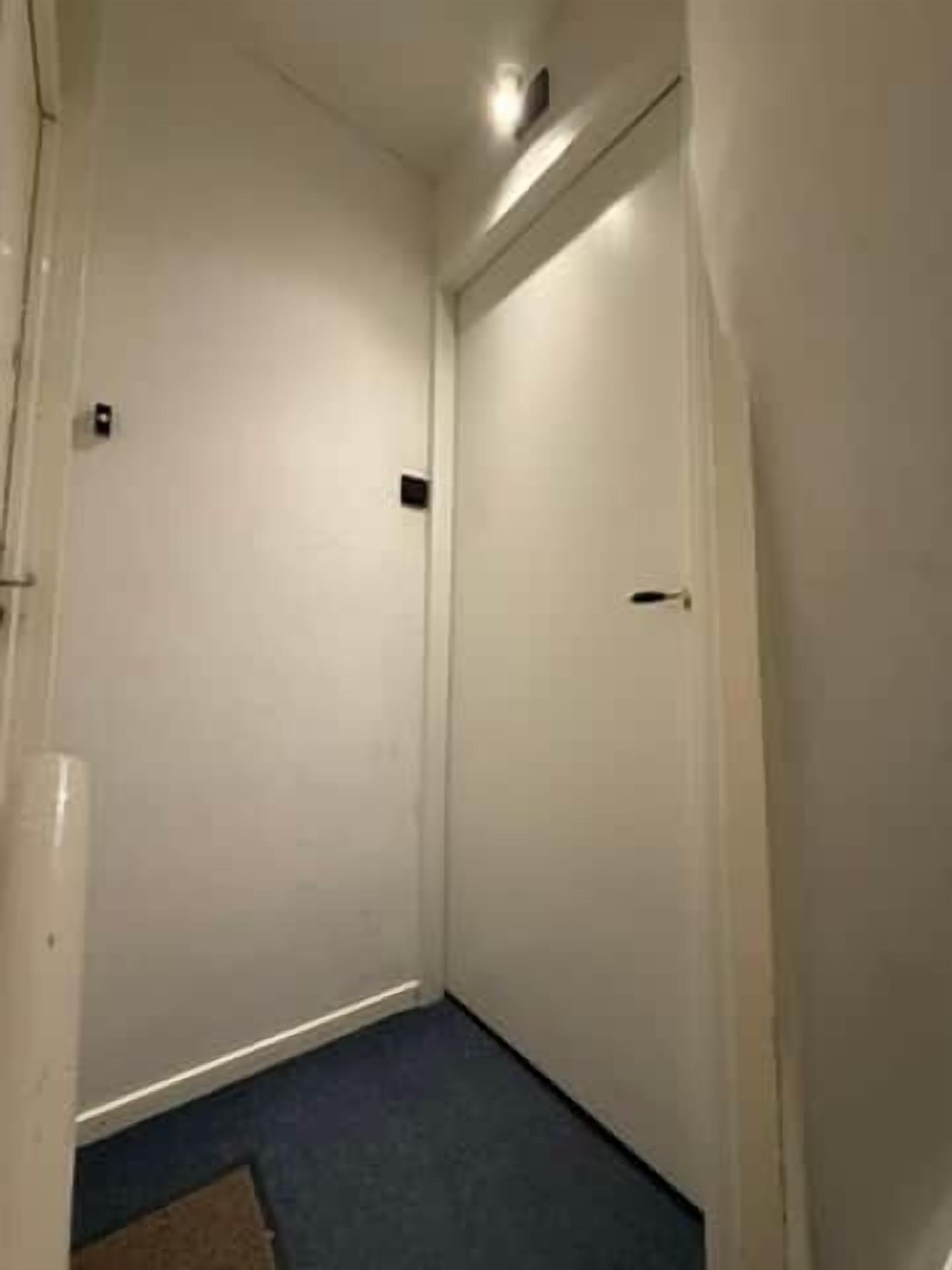 A narrow hallway with white walls and a blue carpet.