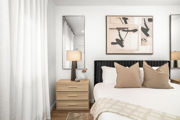Un dormitorio con cama, mesita de noche, espejo y un cuadro en la pared.