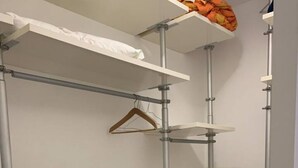 A walk-in closet with open shelving, a hanging rod, and a small stool. - Cozy and bright apartment ideal for two people (Milano)
