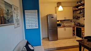 A compact living space with a sofa, a dining table, a kitchen with a refrigerator, and a pendant light. - Cozy and bright apartment ideal for two people (Milano)