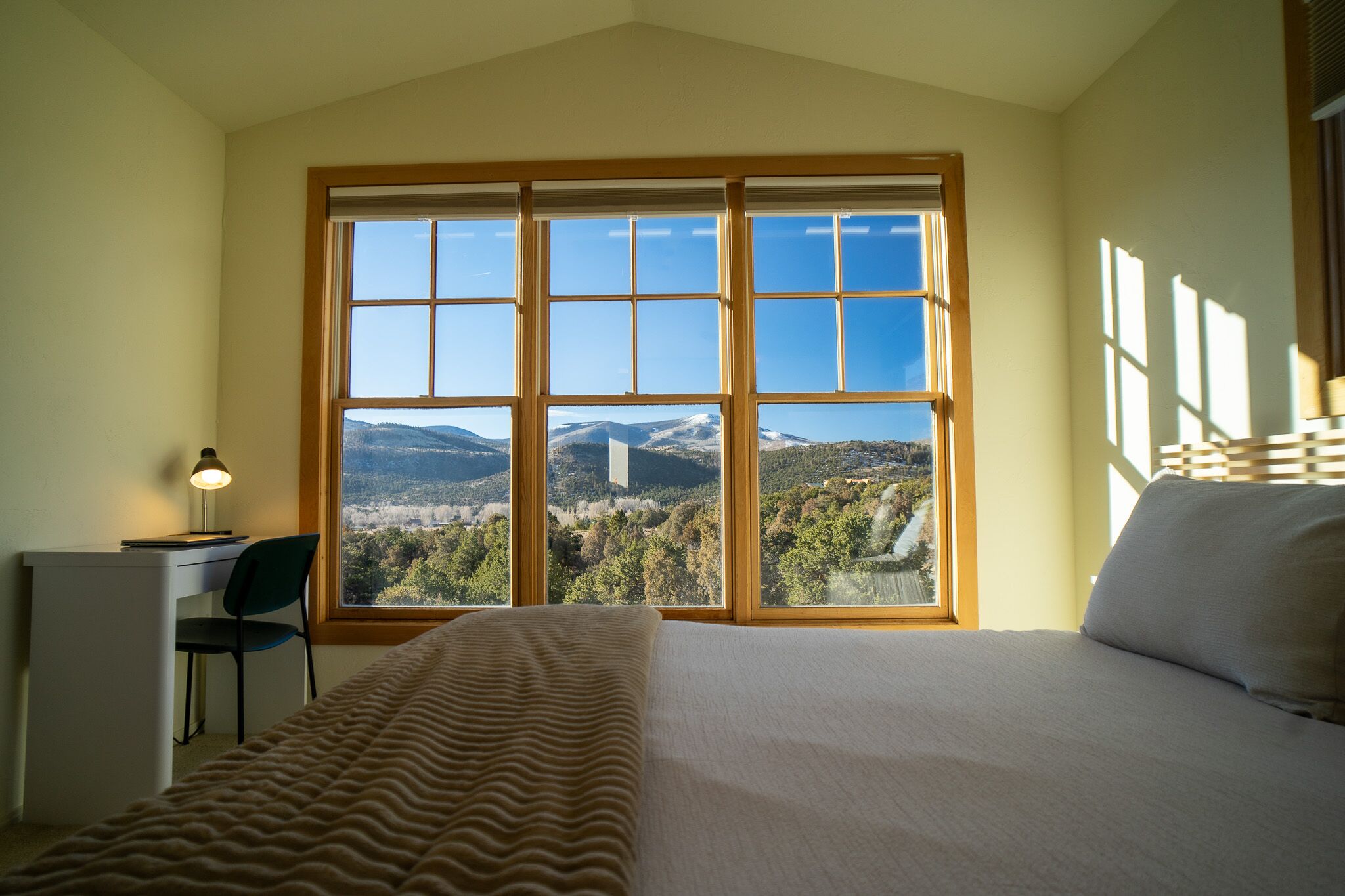 A bedroom with a large window, a bed, a desk, and a chair.