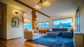 A spacious living room with wooden flooring, a large window offering a mountain view, a rustic tree trunk centerpiece, and a cozy seating area with a sofa and armchairs. - Unbeatable 🏔️  Views, Serene, Fall Foliage, Hike, ATV Access (South Fork)