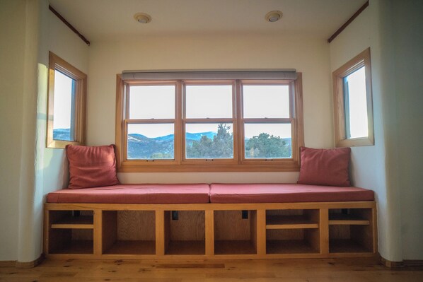 Un banco de madera con cojines y vistas al exterior a través de un ventanal.