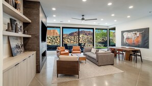 A spacious living room with a fireplace, comfortable seating, and large windows offering a view of a mountainous landscape. - Beautiful Home Near Snow Canyon, Tuacahn, and Black Desert Resort (Ivins)