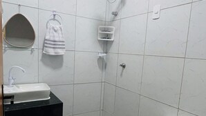 Un baño pequeño y limpio con azulejos blancos, inodoro, lavamanos, ducha y toallero.
