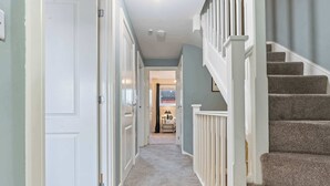 Un pasillo con escaleras alfombradas, puertas blancas y vista a otra habitación.