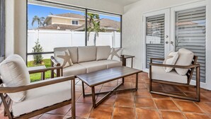 Un patio iluminado por el sol con un sofá color crema, dos sillones y una pequeña mesa.