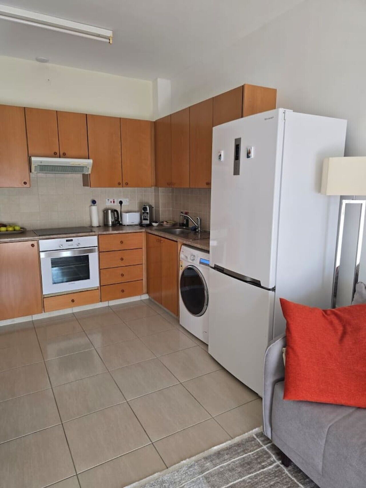 A compact kitchen with wooden cabinets, a built-in oven, a washing machine, and a refrigerator.