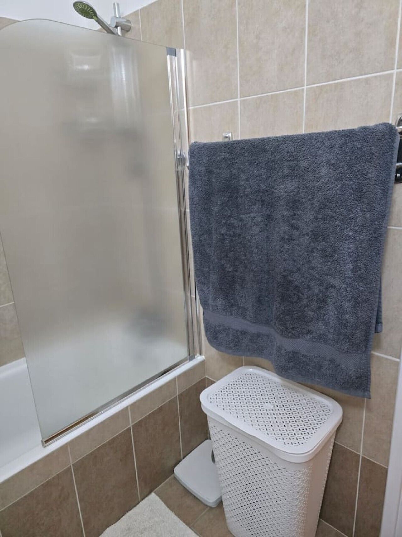 A bathroom with a shower enclosure, a towel rack, and a laundry basket.