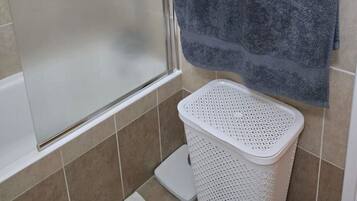 A bathroom with a shower enclosure, a towel rack, and a laundry basket.