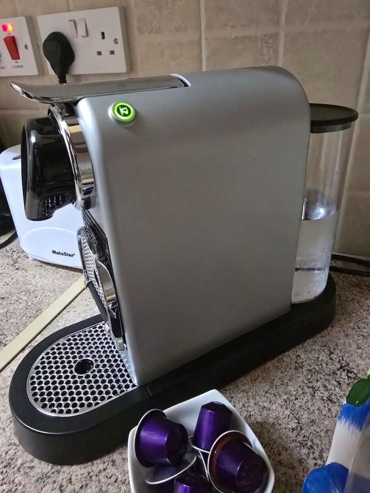 Une machine à café dotée d’un panneau de commande, d’un réservoir d’eau et d’une soucoupe contenant des tasses violettes.