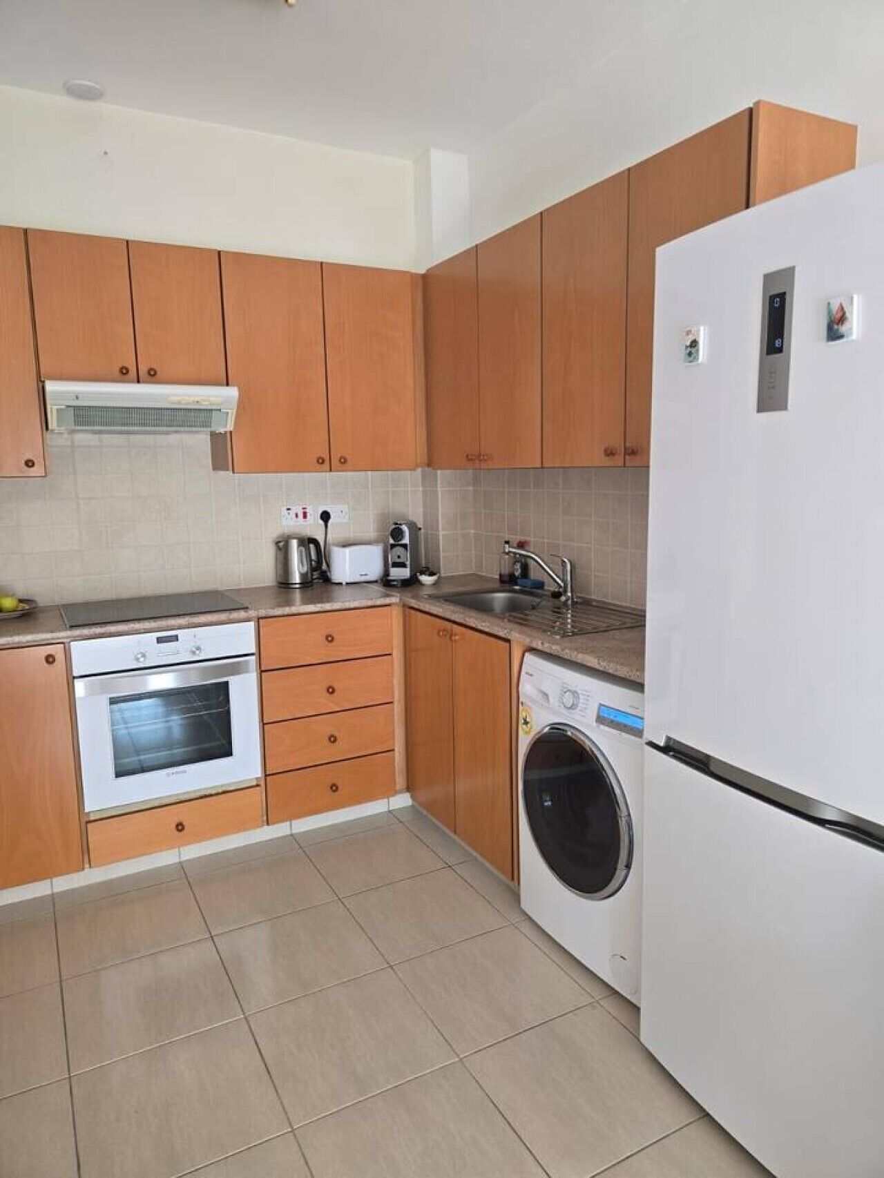 Una cocina con armarios de madera, horno empotrado, lavadora y refrigerador.
