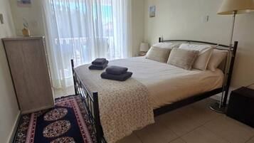 Un dormitorio con cama, ventilador de techo, ventana con cortinas, lámpara de noche y una alfombra decorativa.