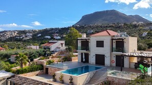 A modern two-story house with a swimming pool, surrounded by greenery and a mountain in the background. - Villa Shlomo-Pool-Near the beach-Kids playground (Plaka)
