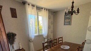 Ein Esszimmer mit Holztisch und -stühlen, einer Kristallleuchtre, einem Fenster mit Vorhängen und einem kleinen Tisch mit Dekorationen.