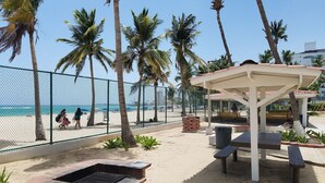 Een terras aan het strand met een barbecue, zitplaatsen en een overdekt gedeelte.