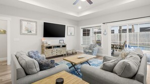 A spacious living room with a ceiling fan, a flat-screen TV mounted on the wall, and a large window with blinds. - Heated Pool - Bachelorette Getaway - Spring Break Sale (Panama City)