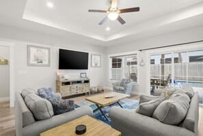 A spacious living room with a ceiling fan, a flat-screen TV mounted on the wall, and a large window with blinds. - Heated Pool - Bachelorette Getaway - Spring Break Sale (Panama City)