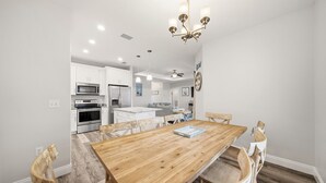A modern kitchen with white cabinets, a wooden dining table, and a chandelier. - Heated Pool - Bachelorette Getaway - Spring Break Sale (Panama City)