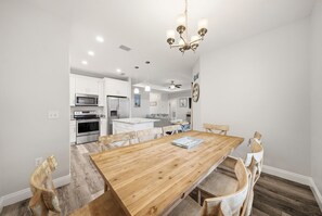 A modern kitchen with white cabinets, a wooden dining table, and a chandelier. - Heated Pool - Bachelorette Getaway - Spring Break Sale (Panama City)