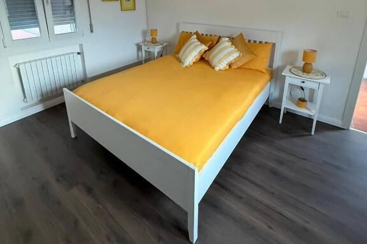 Un dormitorio con una cama, una mesita de noche, una lámpara y una ventana.