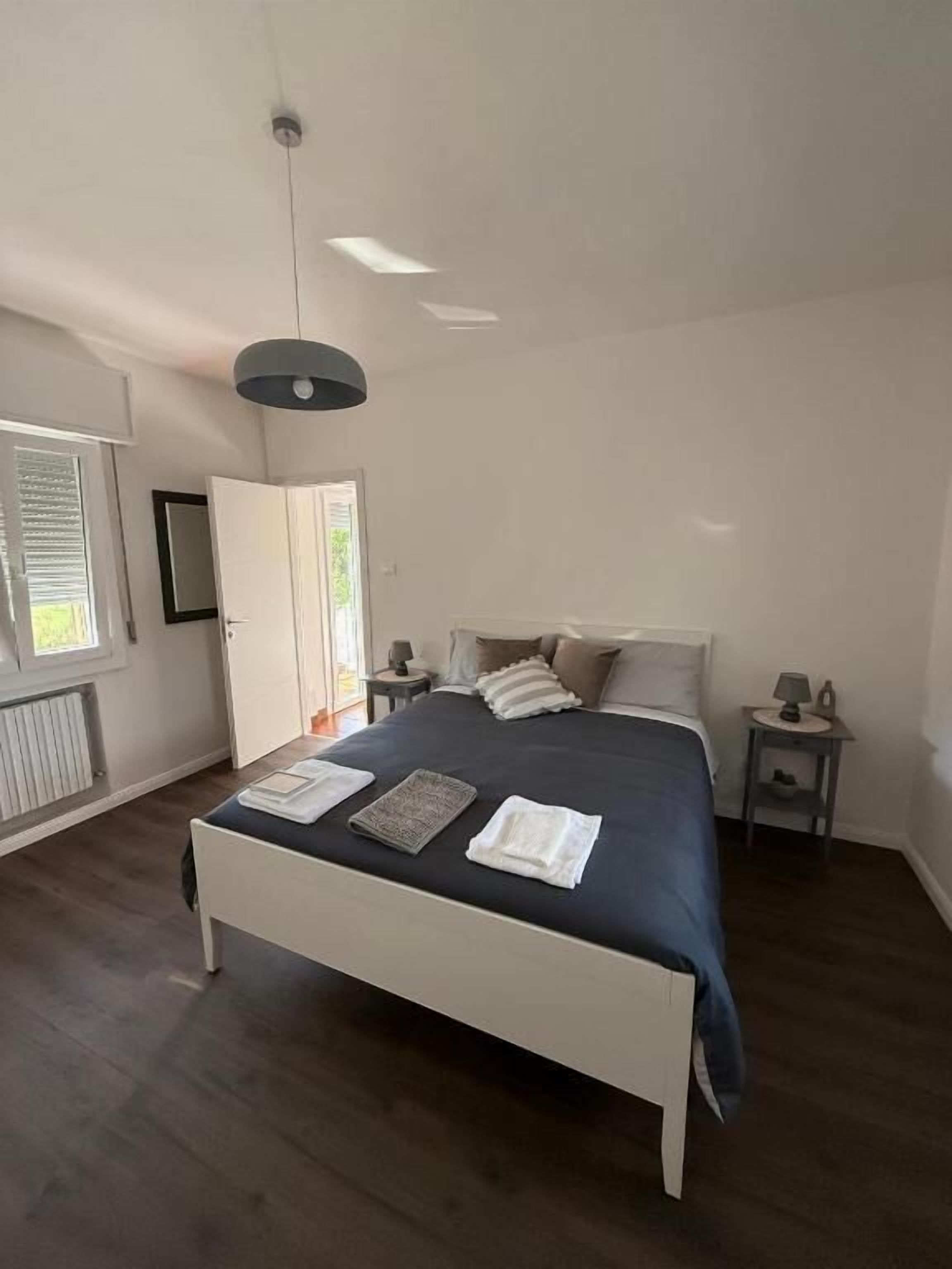 A bedroom with a large bed, a bedside table, a nightstand, a ceiling light, and a window with blinds.