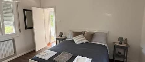 A bedroom with a large bed, a bedside table, a nightstand, a ceiling light, and a window with blinds.