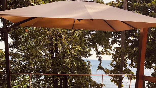 Eine Holzterrasse mit einer Hängematte und Kissen, mit Blick auf ein Gewässer.
