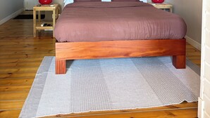 Ein Schlafzimmer mit einem hölzernen Bett, einem Deckenventilator, einem Nachttisch mit einer roten Lampe und einem gerahmten Spiegel an der Wand.