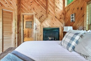 Ein gemütliches Zimmer aus Holz mit einem Bett, einem Kamin und einem Fenster mit Jalousien.